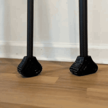 Two 3D-printed prosthetic feet on carbon-fiber posts flexing as they press into a wooden floor.